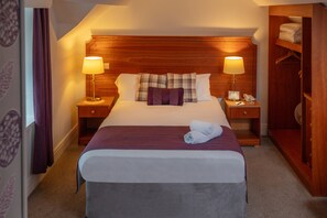 Ein ordentlich bezogenes Bett mit Holz-Kopfstück, zwei Nachttischlampen, einem Telefon am Nachttisch und einem Holzschrank.
