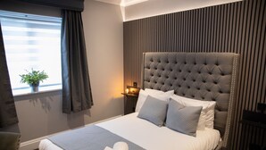 A neatly made bed with a grey headboard, a bedside lamp, and a window with curtains.