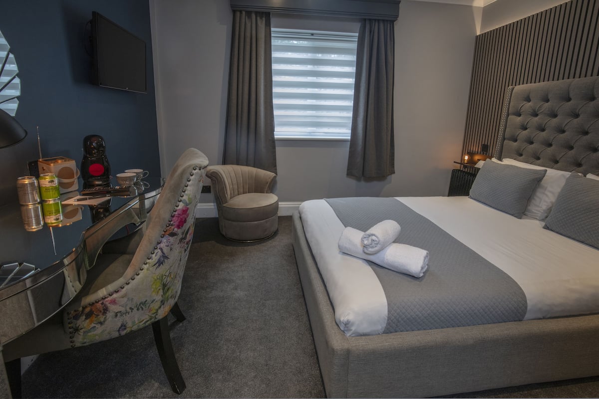 Una habitación de hotel moderna con una cama grande, un escritorio con silla, un televisor y una ventana con cortinas.