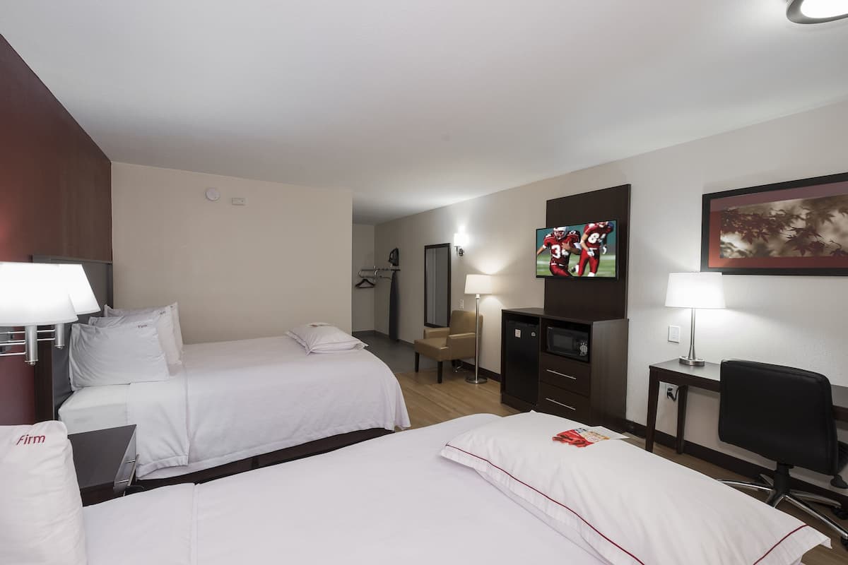 Quarto de hotel com duas camas, uma escrivaninha, uma cadeira, uma televisão e um abajur.