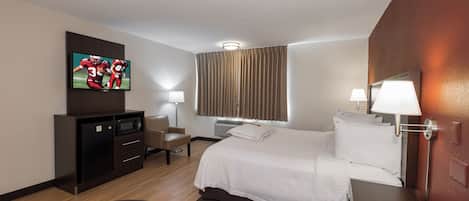 Una habitación de hotel con cama, escritorio, televisión, silla y lámpara.