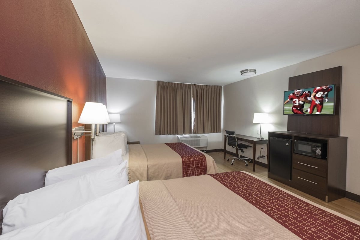 Quarto de hotel com duas camas, uma escrivaninha, televisão e minibar.
