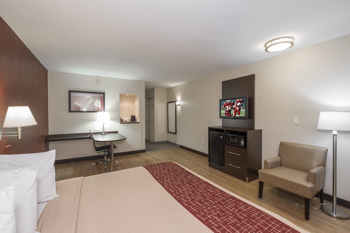 A hotel room with a bed, desk, chair, TV, and a small kitchenette.