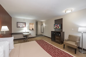 Une chambre d’hôtel équipée d’un lit, d’un bureau, d’une chaise, d’une télévision et d’une petite kitchenette.