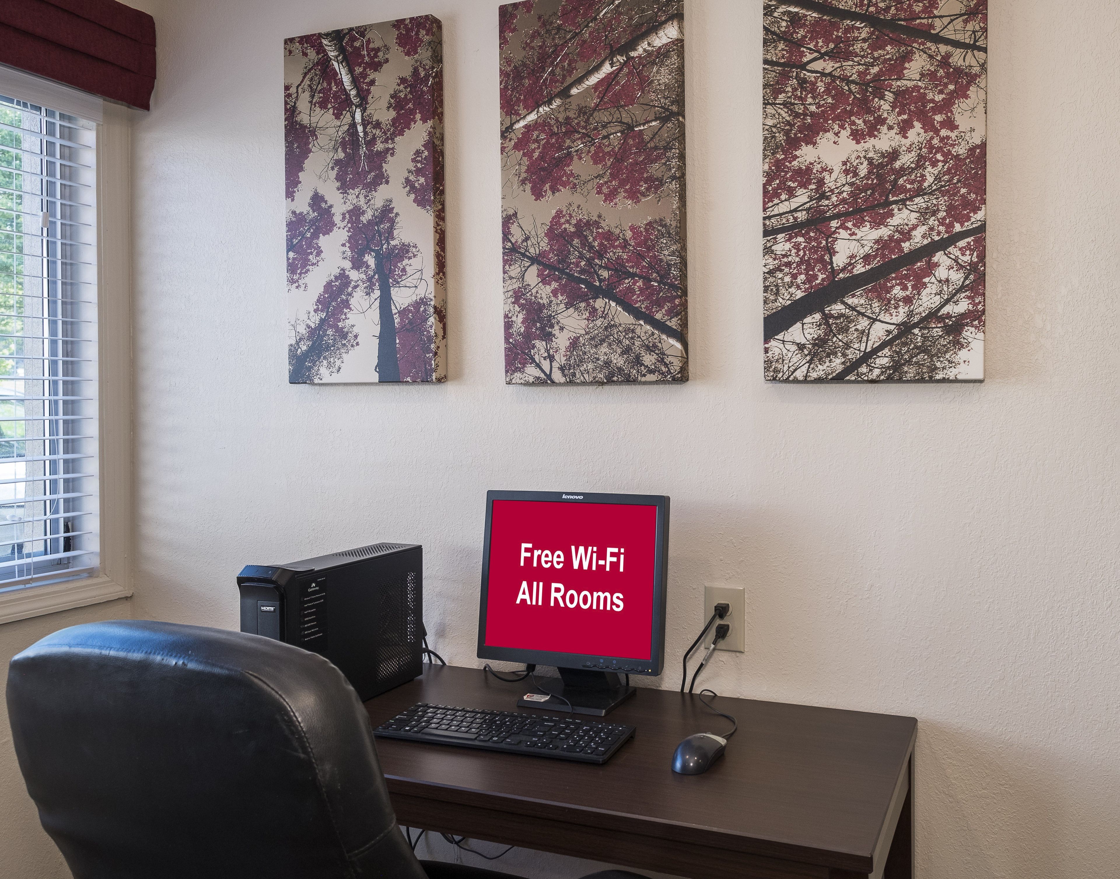 A workspace with a desktop computer, a keyboard, a mouse, and a monitor displaying 'Free Wi-Fi All Rooms'.