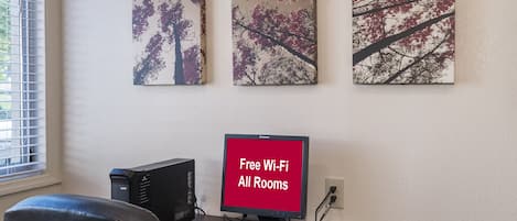 Ein Arbeitsplatz mit einem Schreibtischcomputer, einer Tastatur, einer Maus und einem Bildschirm, der 'Kostenloses WLAN in allen Zimmern' anzeigt.