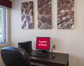 A workspace with a desktop computer, a keyboard, a mouse, and a monitor displaying 'Free Wi-Fi All Rooms'. - Red Roof Inn PLUS+ Poughkeepsie (Poughkeepsie)