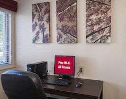 Un espacio de trabajo con computadora de escritorio, teclado, ratón y monitor que muestra 'Wi-Fi gratis en todas las habitaciones'.