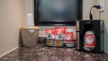 A coffee machine, a trash bin, and a basket with coffee packets on a marble countertop.
