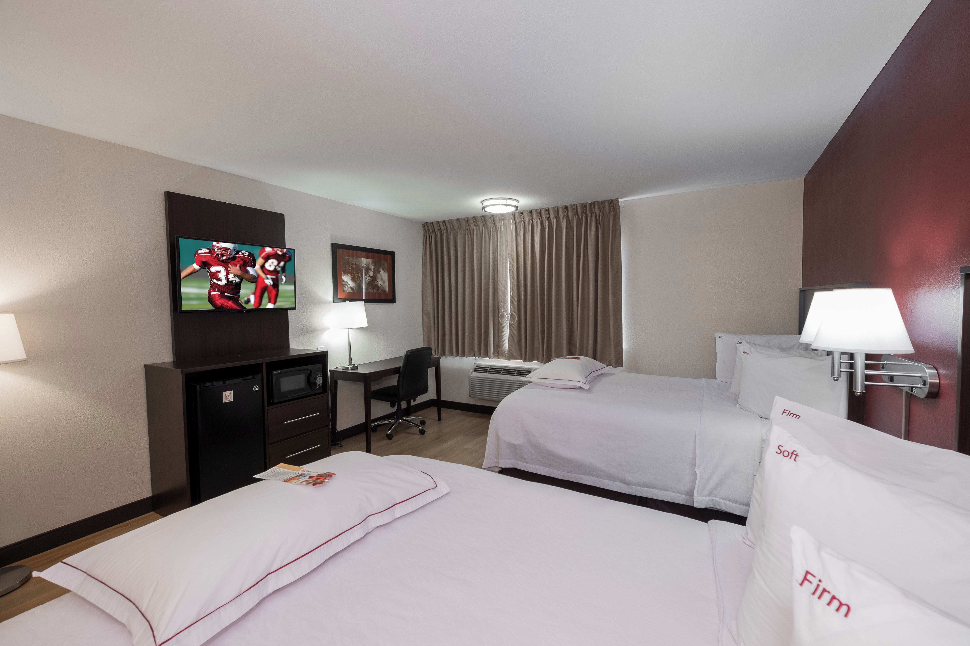 A hotel room with two beds, a desk, a television, and a window with curtains.