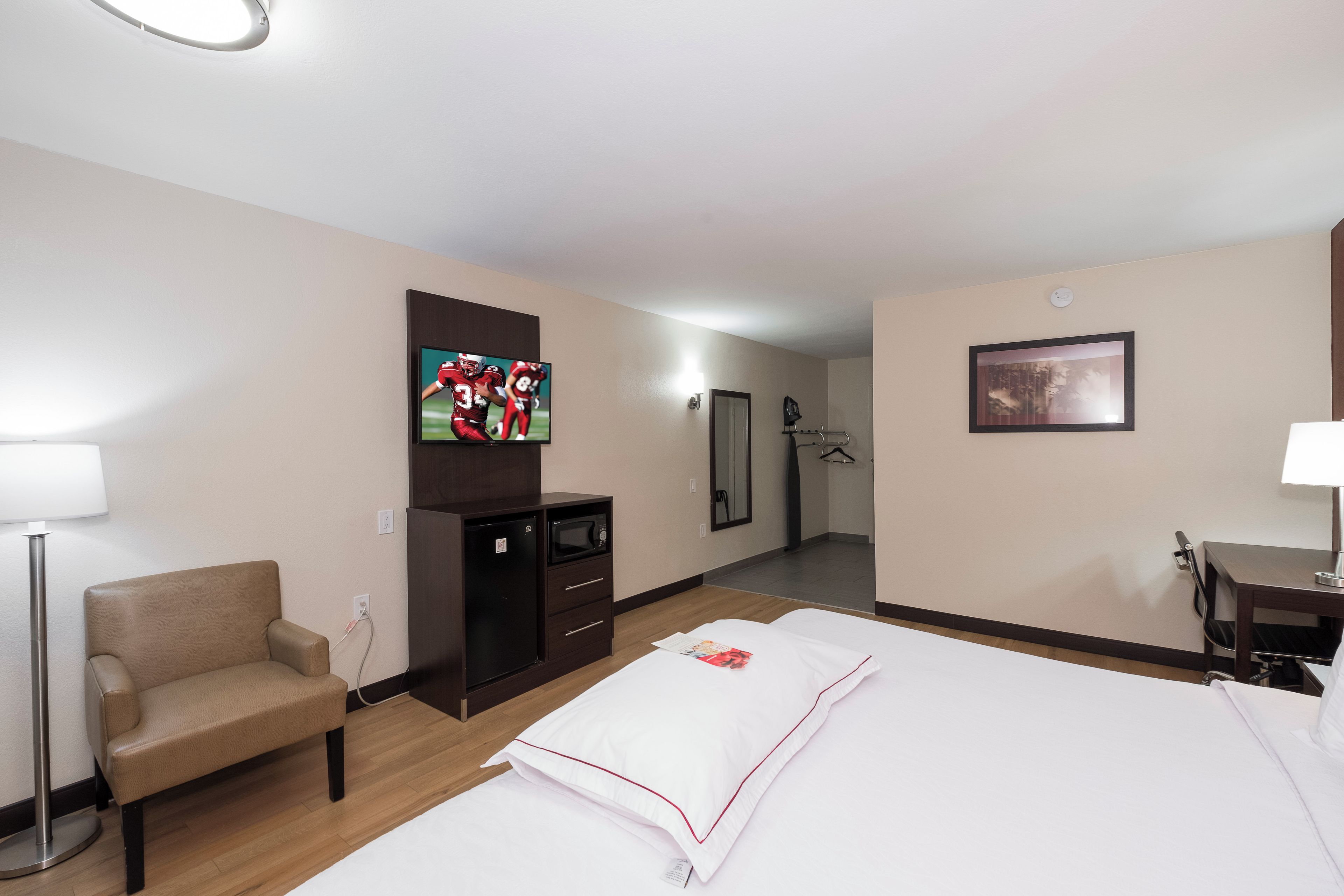 Habitación de hotel con cama, televisor, escritorio, silla, microondas y espejo.