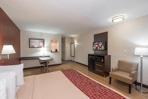 Habitación de hotel con cama, escritorio, silla, televisor y una kitchenette pequeña.