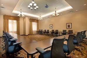A conference room with a long table, rows of chairs, and chandeliers.