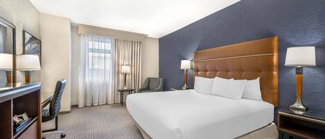 A hotel room with a large bed, a desk with a chair, a small table, and a lamp.
