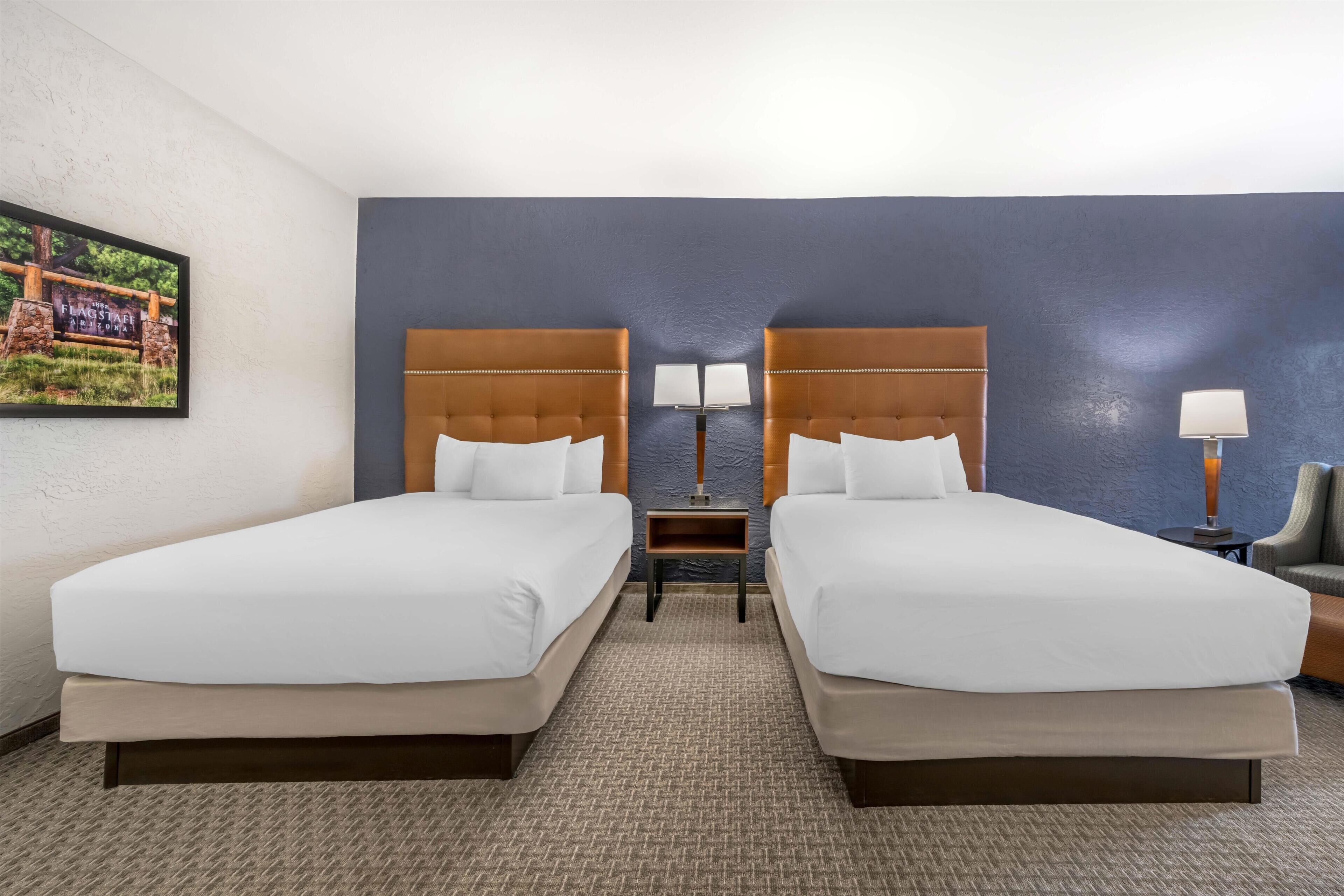 A hotel room with two beds, a nightstand, a lamp, and a chair.