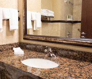 A bathroom with a granite countertop, a sink, and a mirror reflecting a shower area.