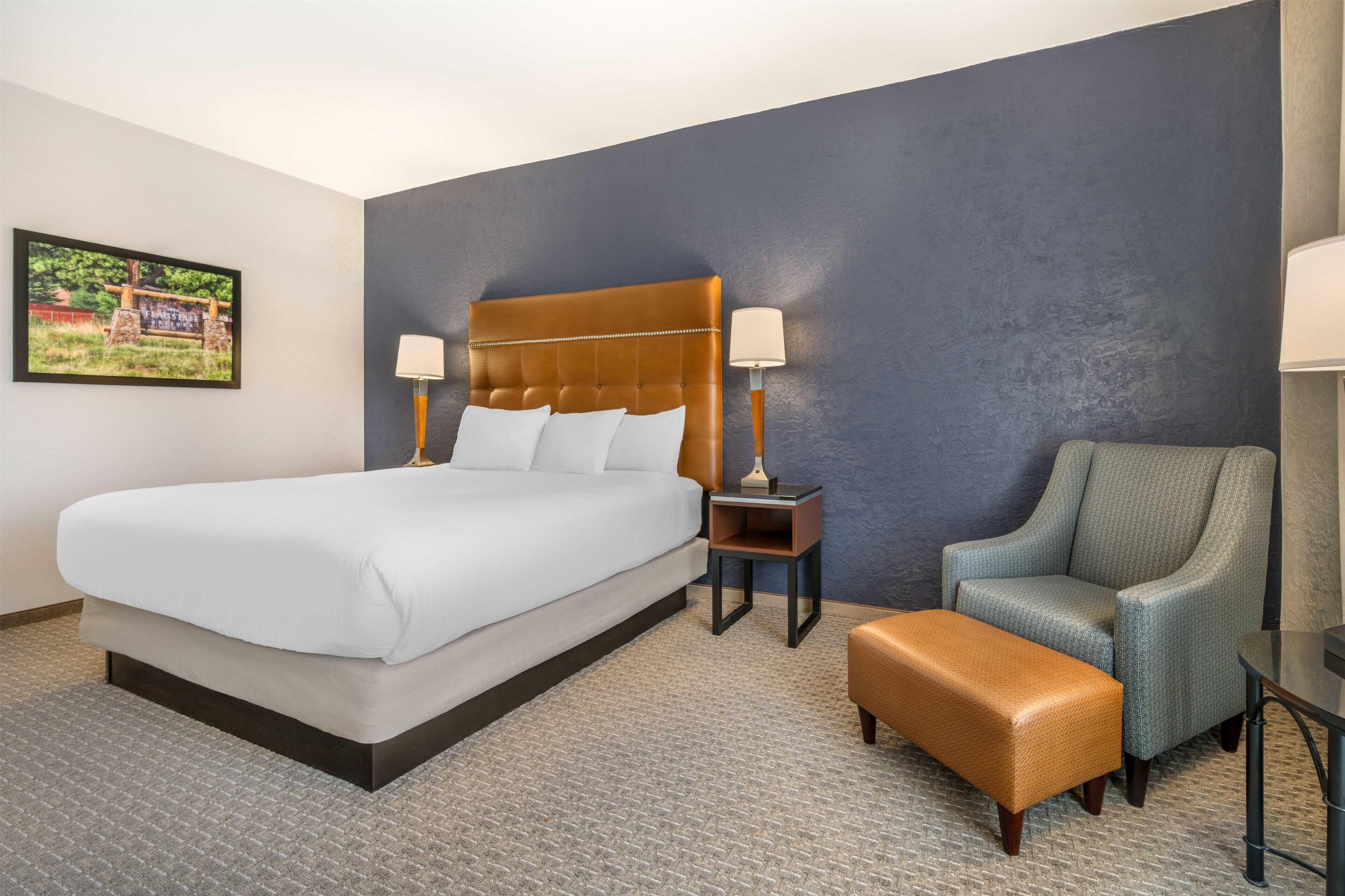 A hotel room with a large bed, a chair, a small table, and a nightstand.