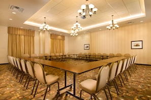 A conference room with a long table surrounded by chairs, a chandelier, and patterned carpet.