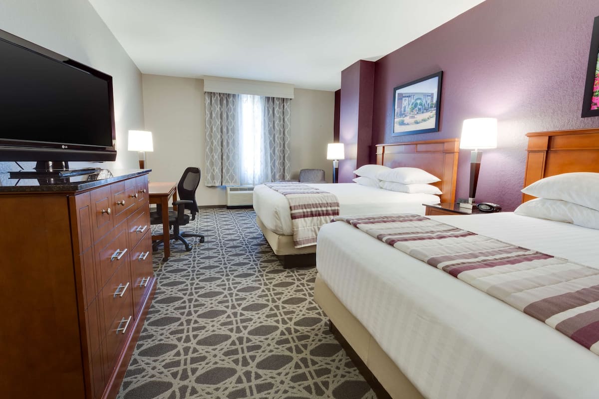 A hotel room with a large flat-screen TV, two beds, a desk, and a chair.