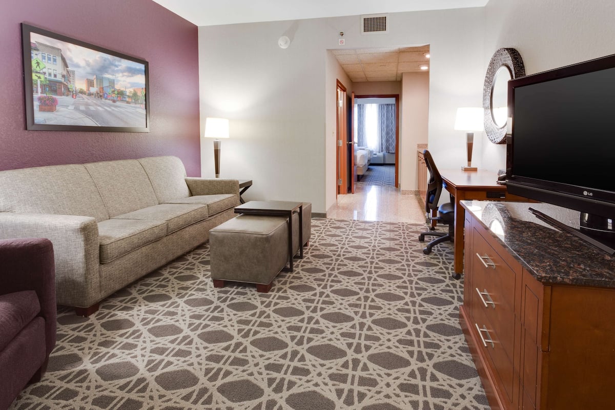 A hotel room with a sofa, ottoman, TV, and a patterned rug.