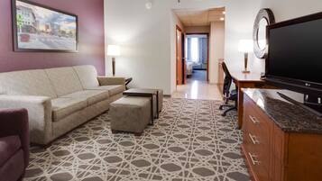 Habitación de hotel con sofá, reposapiés, televisor y alfombra estampada.