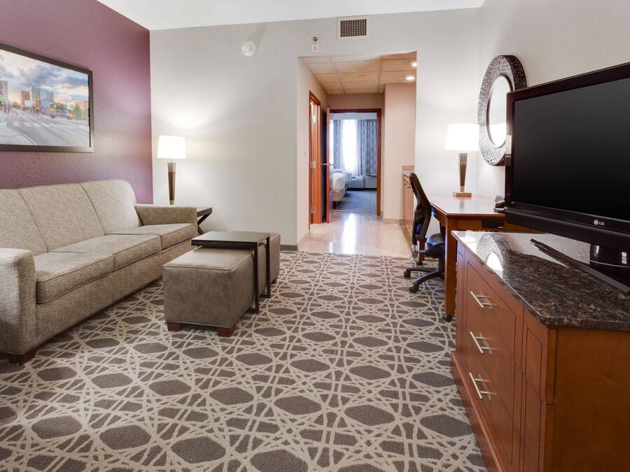 Habitación de hotel con sofá, reposapiés, televisor y alfombra estampada.