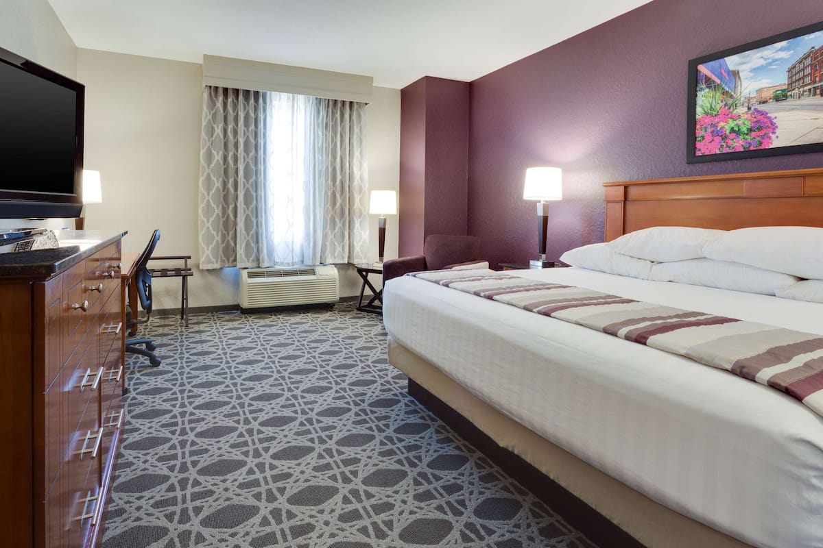 A hotel room with a large bed, a TV, a desk with a chair, and a window with curtains.