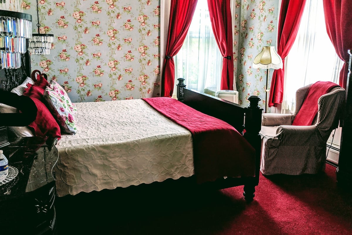 A bedroom with a bed, a chair, a dresser, and a lamp.