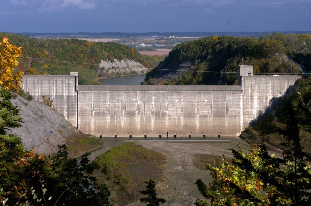 Een grote dam met een betonnen overloop en een rivier eronder.
