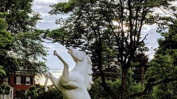 An equestrian statue stands proudly in a serene park setting surrounded by trees and a historic brick building.