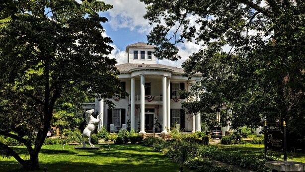 A large, two-story house with a symmetrical facade, large columns at the entrance, and a well-maintained garden with a statue. - Allegiance Bed and Breakfast (Mount Morris)