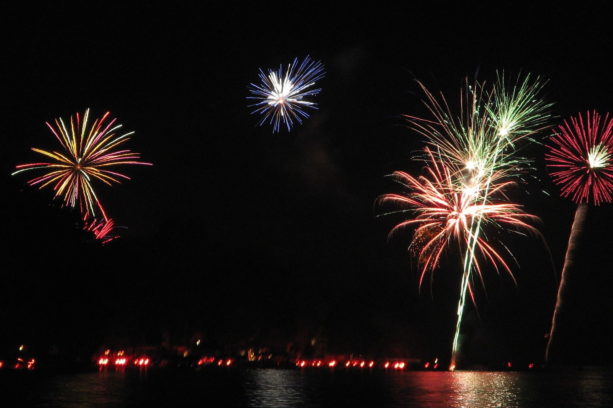 Una vista nocturna de fuegos artificiales sobre el agua, con reflejos en la superficie.
