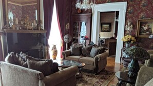 A traditional living room with a fireplace, comfortable seating, and a chandelier. - Allegiance Bed and Breakfast (Mount Morris)