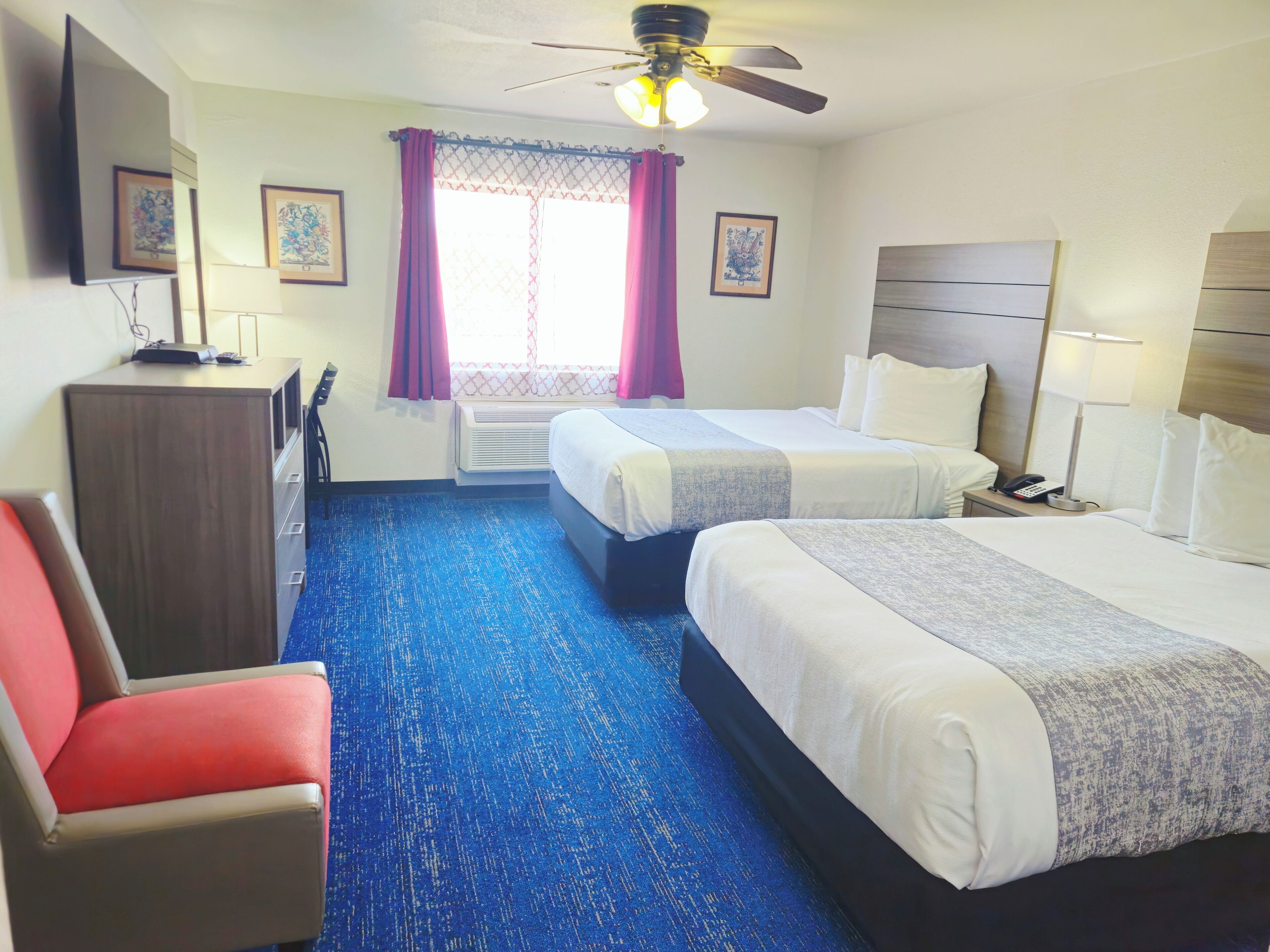 Ein Hotelzimmer mit zwei Betten, einem Schreibtisch, einem Sessel und Bildern an der Wand.