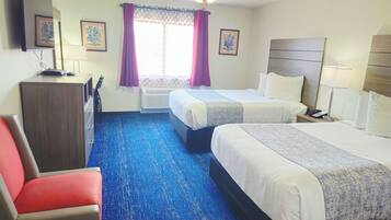 Ein Hotelzimmer mit zwei Betten, einem Schreibtisch, einem Sessel und Bildern an der Wand.