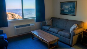 A living room with a view of the sea, a sofa, a wooden table, and a painting on the wall.