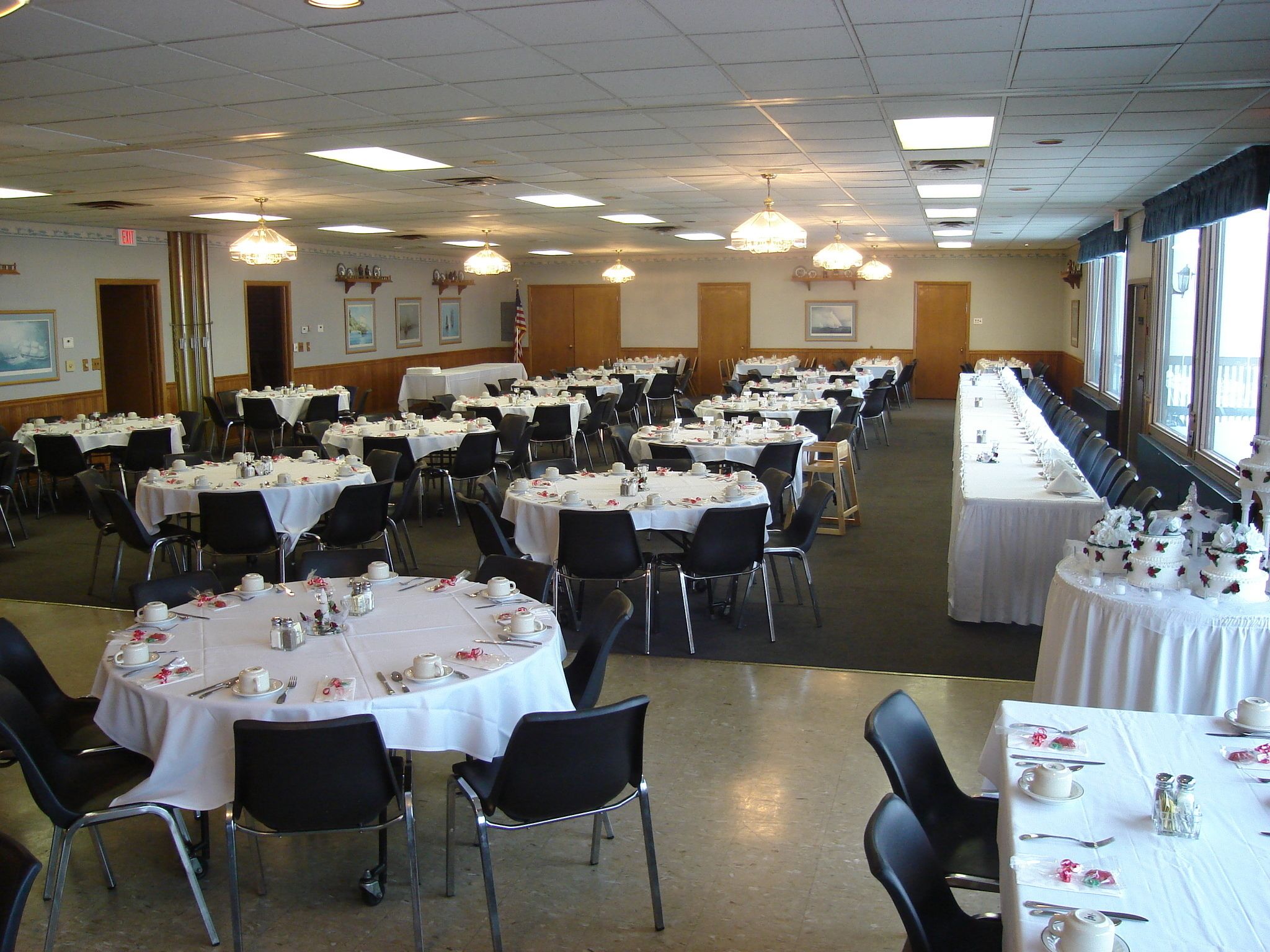A banquet hall with round tables set for dining, featuring white tablecloths and black chairs.