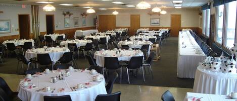 Une salle de banquet avec des tables rondes dressées pour le repas, agrémentées de nappes blanches et de chaises noires.