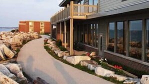 A modern building with large windows, a pathway lined with rocks, and a view of the sea.