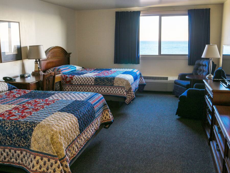 A hotel room with two beds, a desk, a chair, a TV, and a view of the sea.