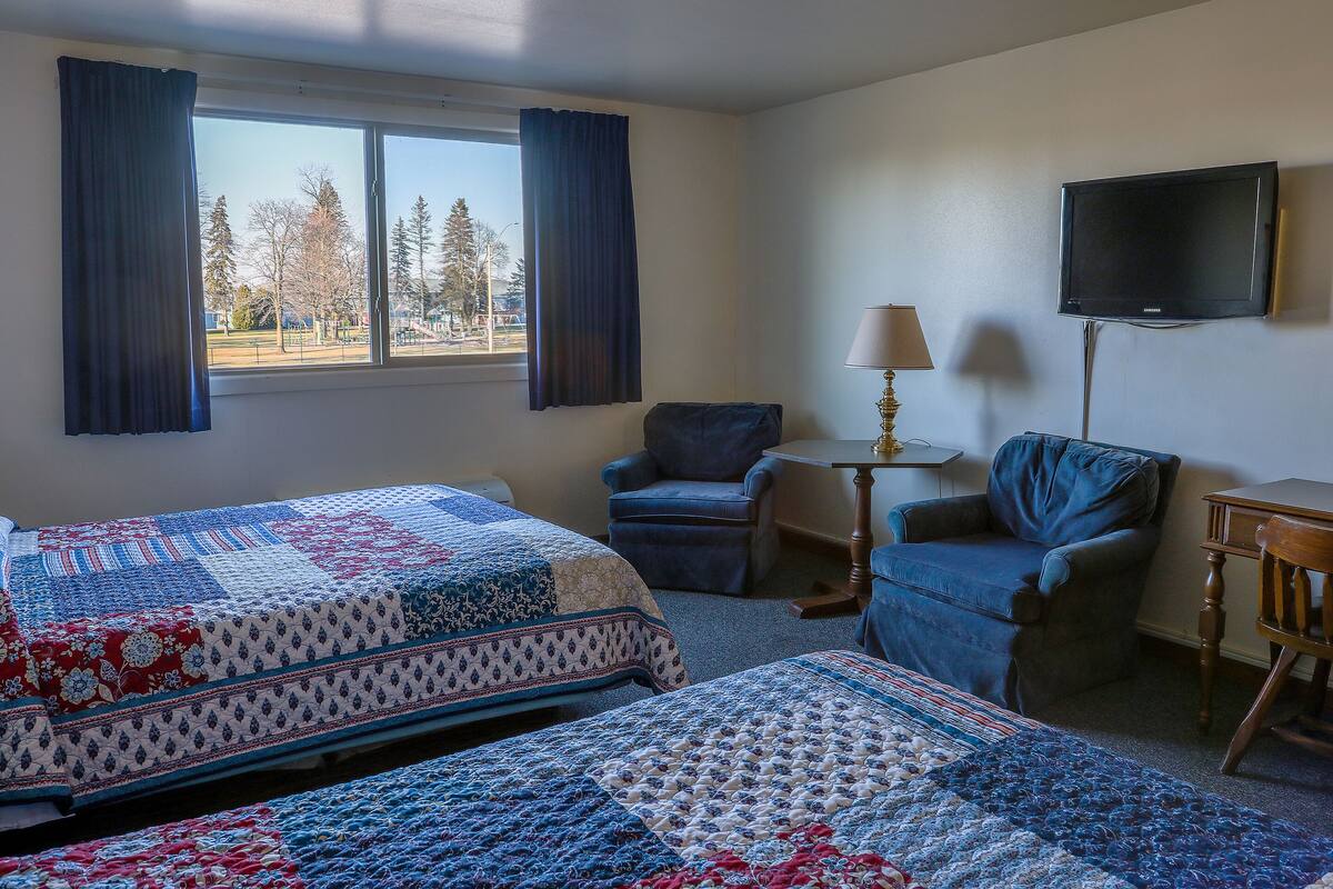 A hotel room with two beds, a TV, a chair, and a lamp.