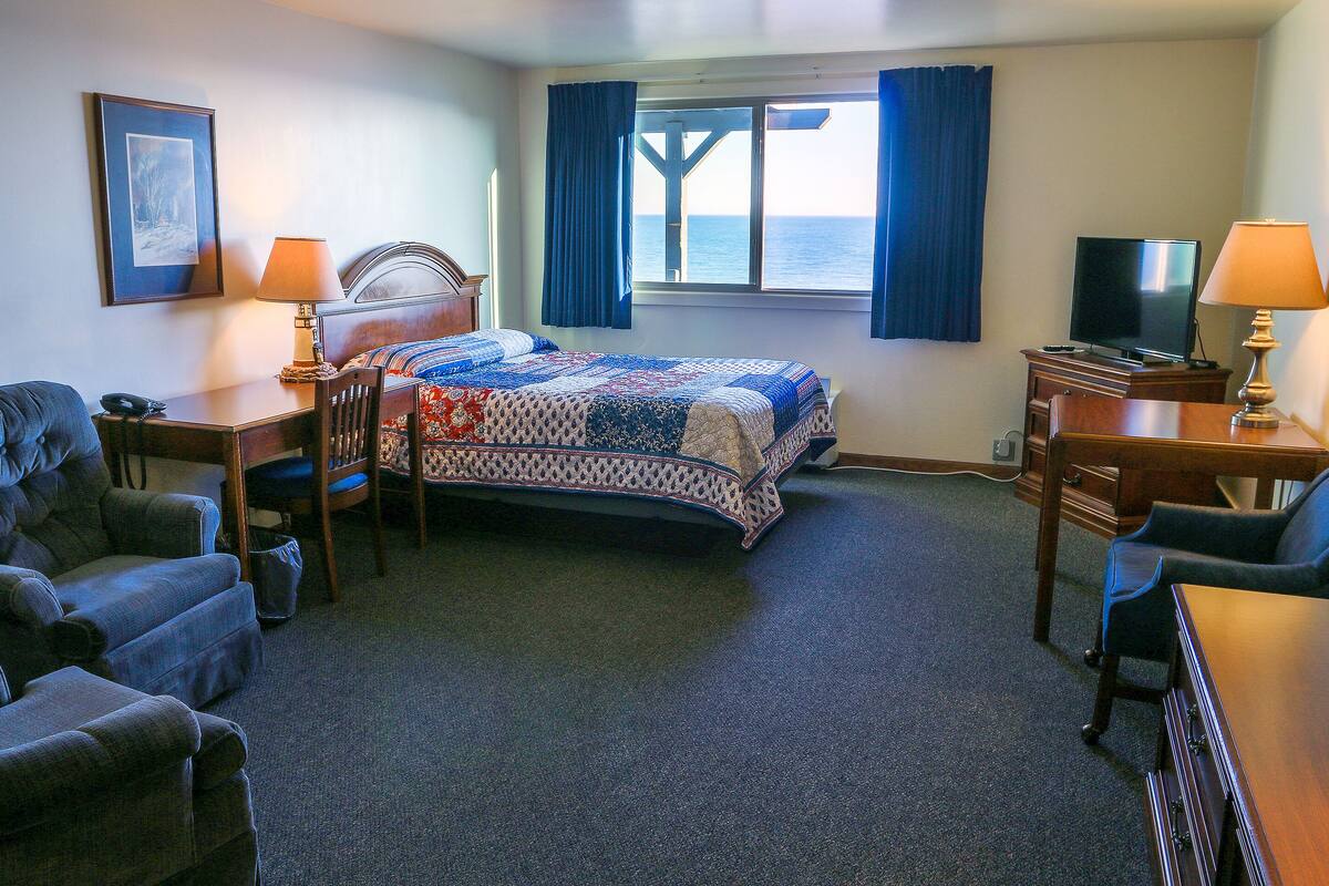A hotel room with a bed, a desk, a chair, a TV, and a window with curtains.