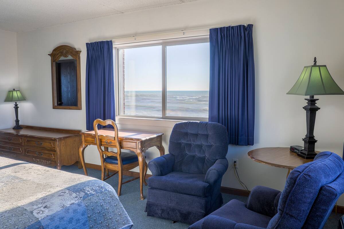A room with a bed, a desk, a chair, and a view of the ocean.