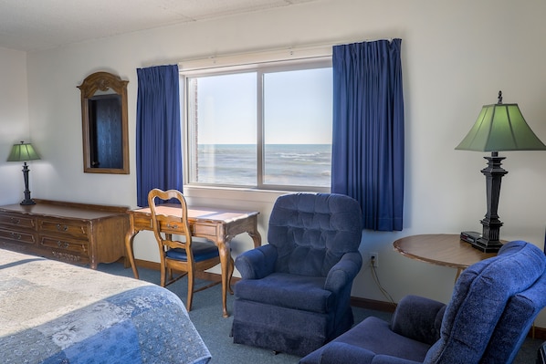 A room with a bed, a desk, a chair, and a view of the ocean.