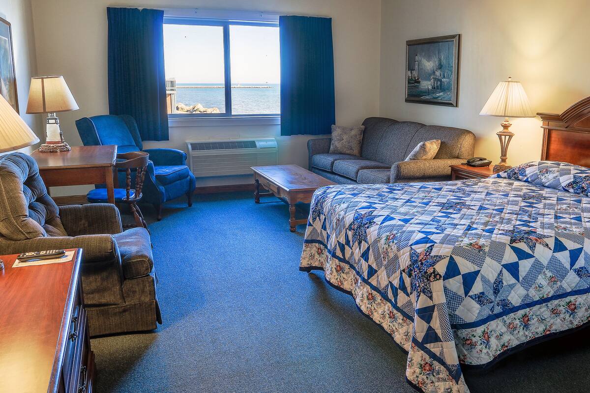 A hotel room with a bed, two sofas, a desk, and a window with a view of the sea.