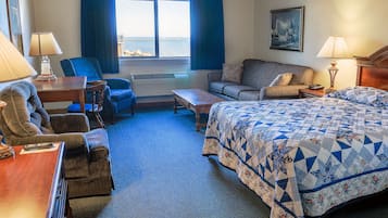 A hotel room with a bed, two sofas, a desk, and a window with a view of the sea.