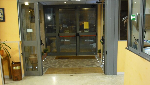 Entrada de hotel con puerta de vidrio, piso de piedra y un pequeño tapete que conduce a la puerta.