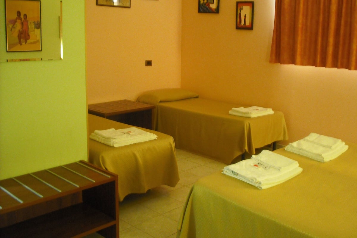 Ein Hotelzimmer mit zwei Einzelbetten, einer kleinen Holzbank und einem Nachttisch.