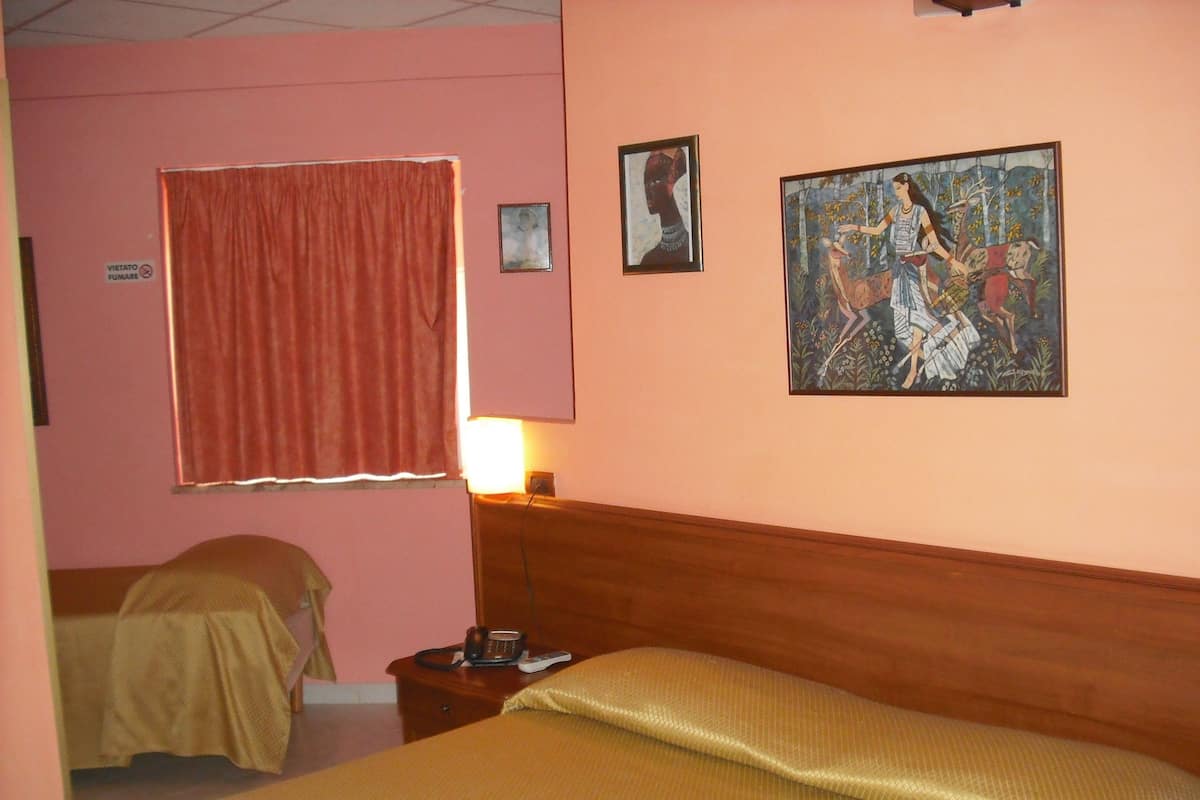 Ein Hotelzimmer mit zwei Betten, einem hölzernen Kopfteil, einem Nachttisch mit Lampe und Bildern an den Wänden.