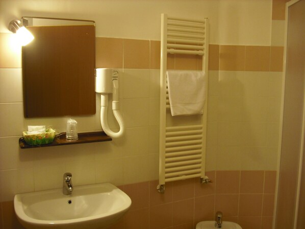 Un baño con lavamanos, espejo, toallero y calefactor.
